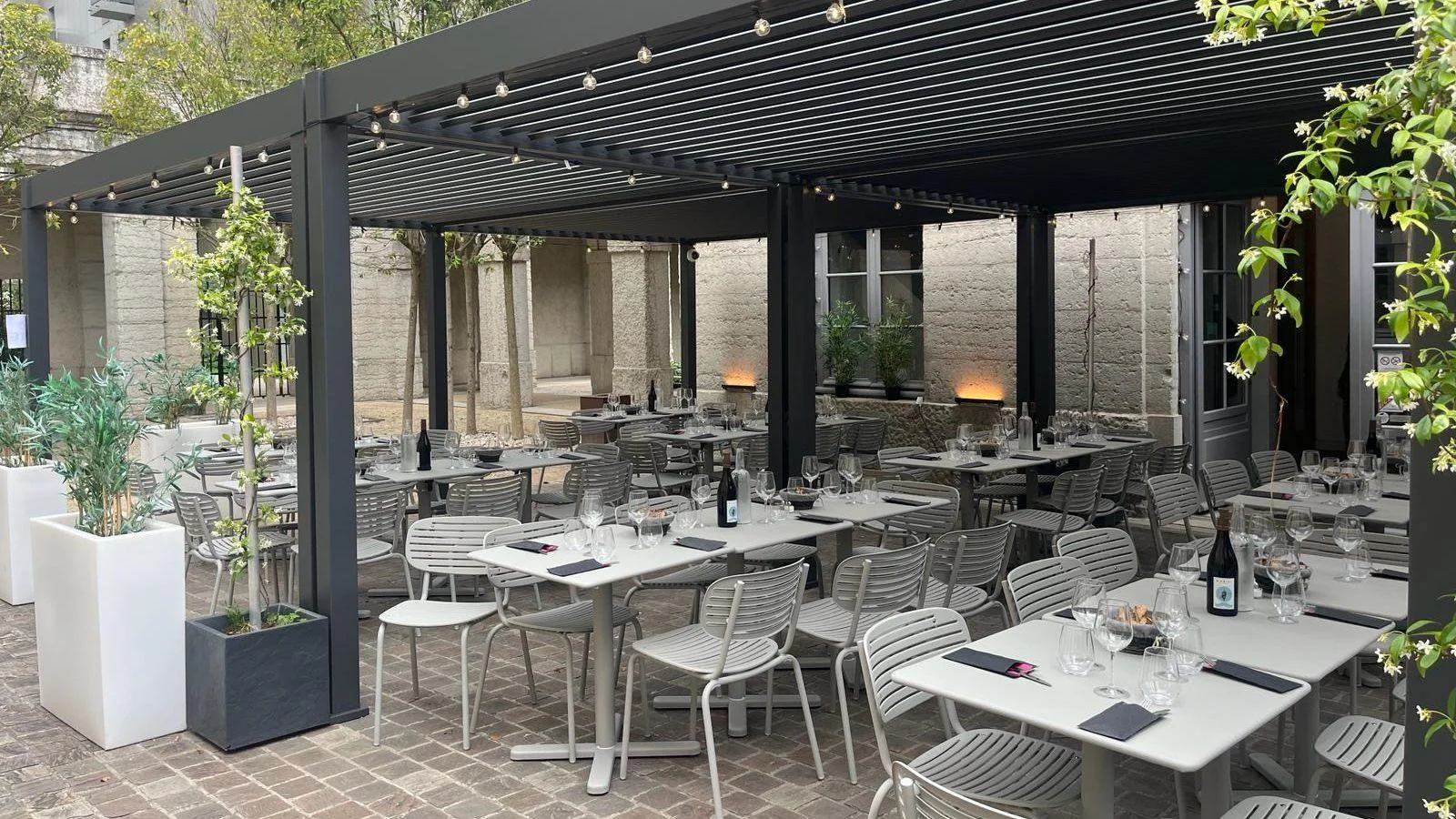 Outdoor restaurant tables and woven chairs beneath a slatted pergola