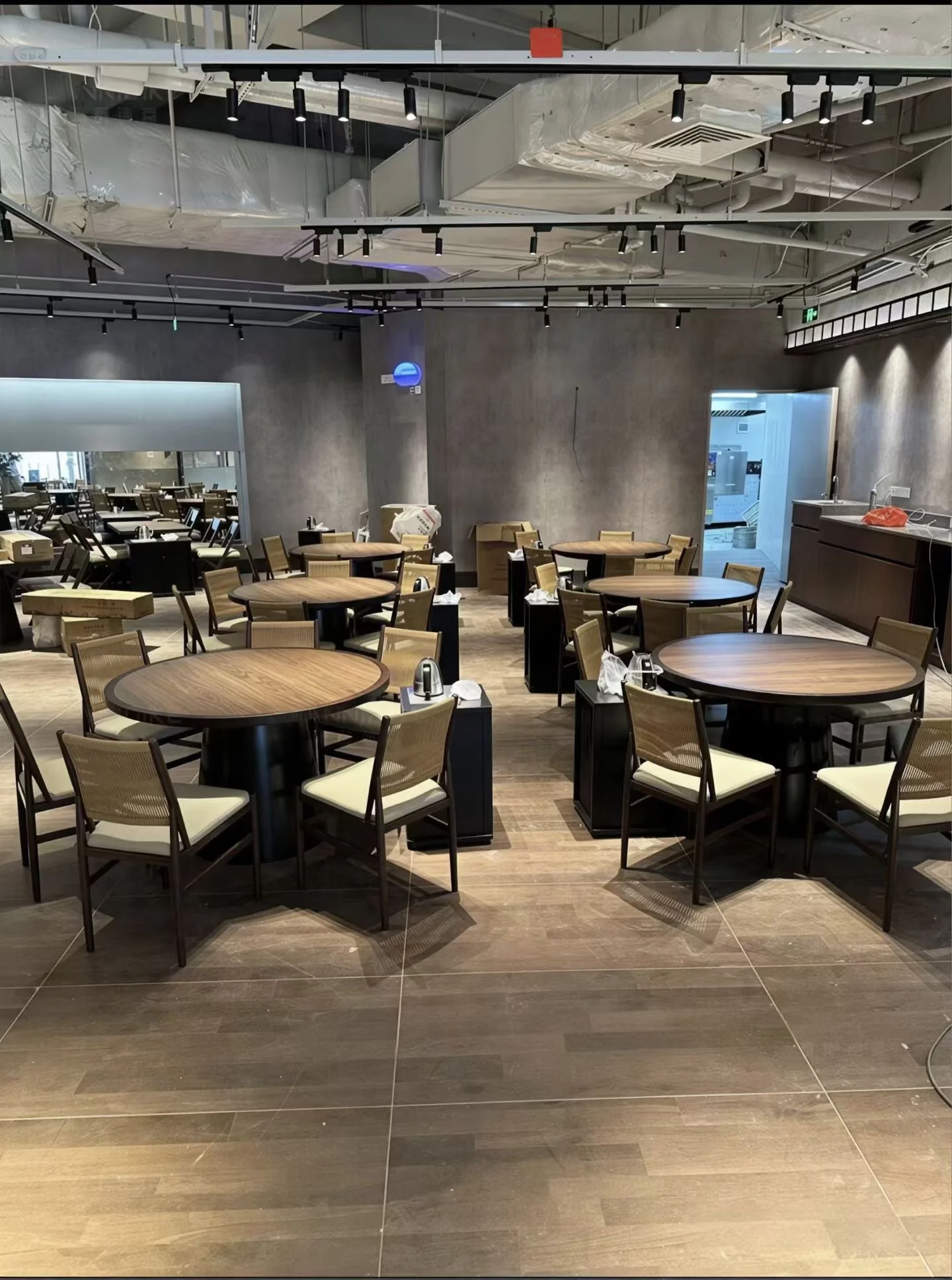 Round wood-grain tables with dark pedestal bases and woven-back dining chairs in a LONGG restaurant project in Canada.