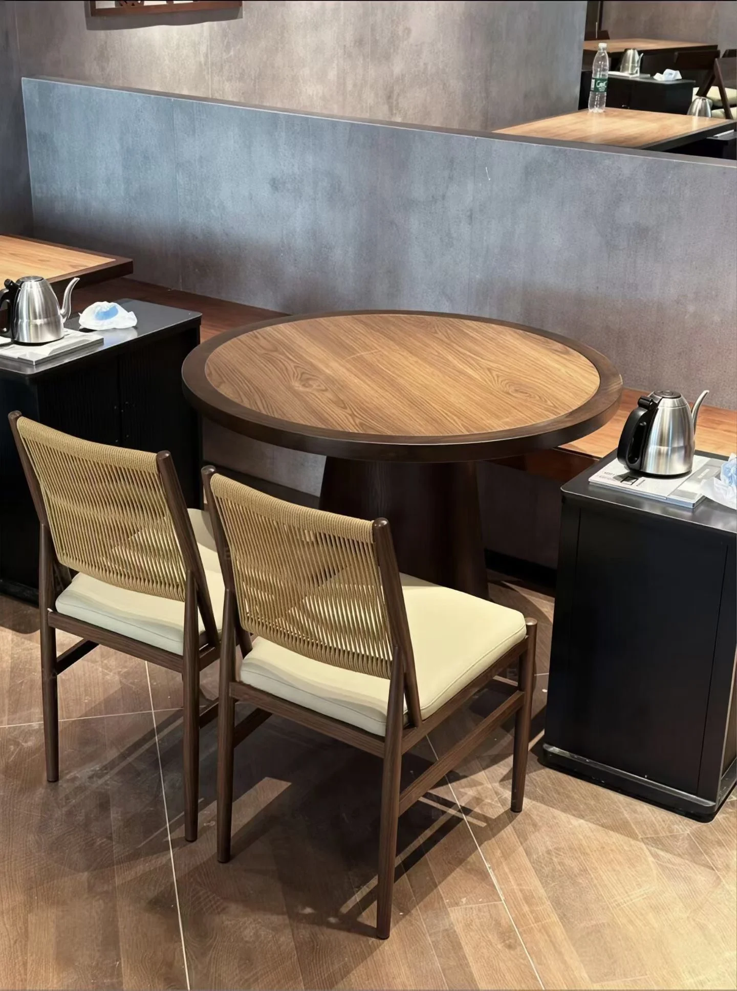 Two dark-brown woven-back chairs with cream cushions beside a round wood-grain table and partition-backed bench.